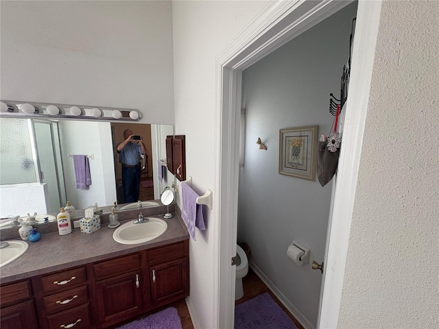 bathroom with double vanity, toilet, a shower with door, and a sink