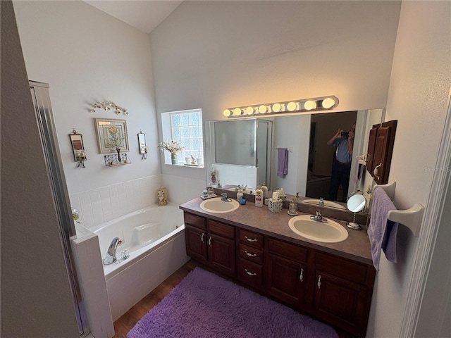 full bath featuring double vanity, wood finished floors, a garden tub, and a sink