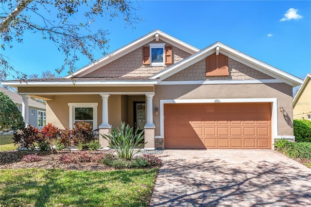 craftsman inspired home featuring a garage, driveway, covered porch, and stucco siding
