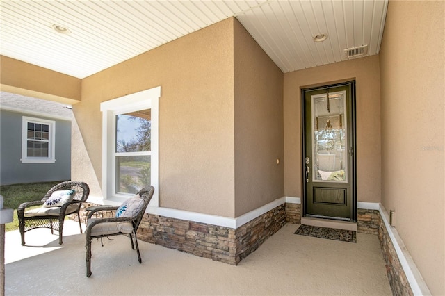 doorway to property with stone siding, visible vents, and stucco siding