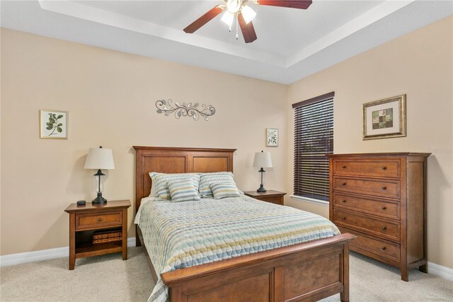 bedroom featuring a raised ceiling, baseboards, light colored carpet, and ceiling fan