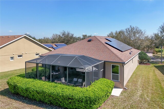 back of property with glass enclosure, roof mounted solar panels, a yard, stucco siding, and roof with shingles