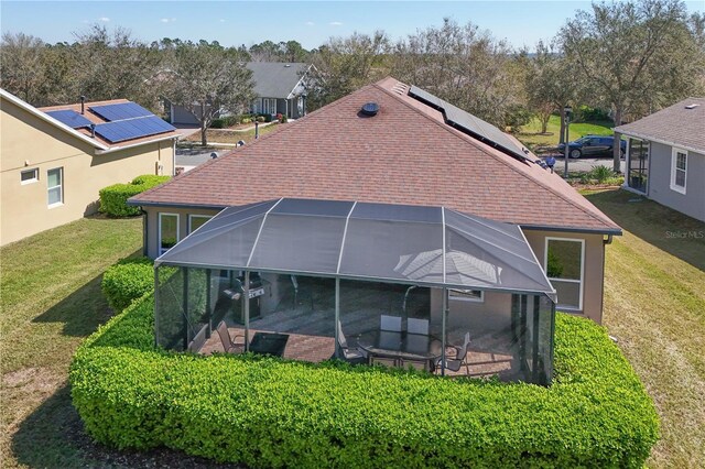 rear view of property with a lawn, solar panels, a lanai, and a shingled roof