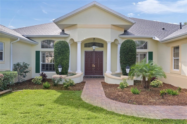 1721 Sunset Ridge Dr, The Villages, FL 32162 - view of exterior entry featuring roof with shingles, stucco siding, a lawn, and a porch