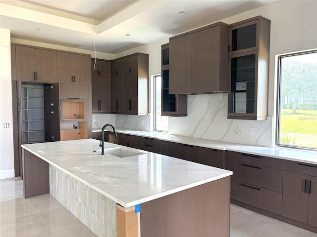 16142 Trivoli Cir, Bella Collina, FL 34756 - kitchen featuring light stone countertops, tasteful backsplash, glass insert cabinets, and a large island with sink