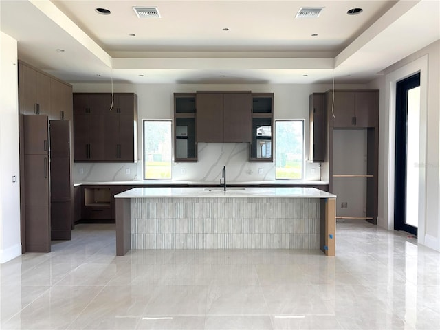 16142 Trivoli Cir, Bella Collina, FL 34756 - kitchen featuring a tray ceiling, light countertops, a kitchen island with sink, and dark brown cabinetry