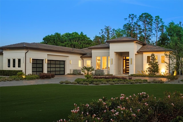 prairie-style house featuring driveway, an attached garage, stucco siding, french doors, and a front lawn
