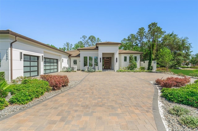 prairie-style home featuring stucco siding, decorative driveway, and a garage