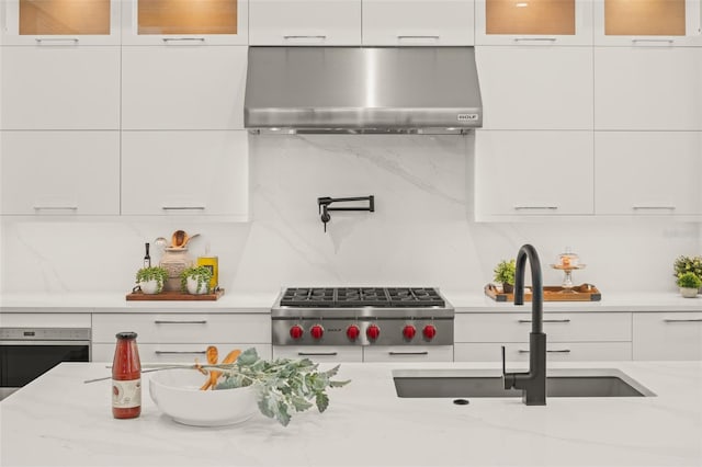 kitchen with a sink, modern cabinets, extractor fan, white cabinets, and appliances with stainless steel finishes