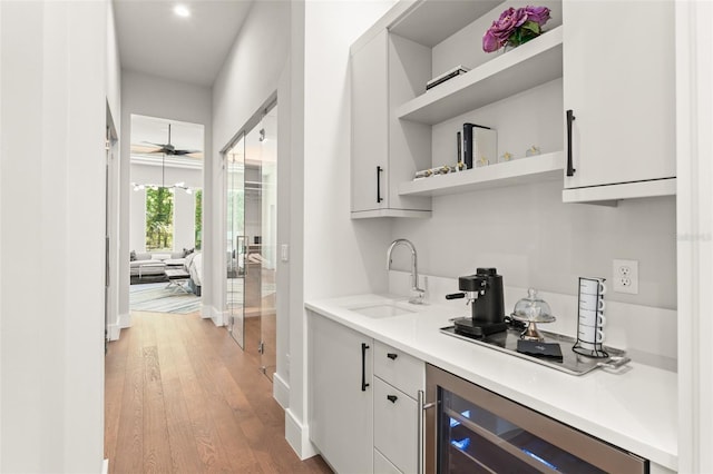 bar with a sink, beverage cooler, light wood-style floors, baseboards, and wet bar