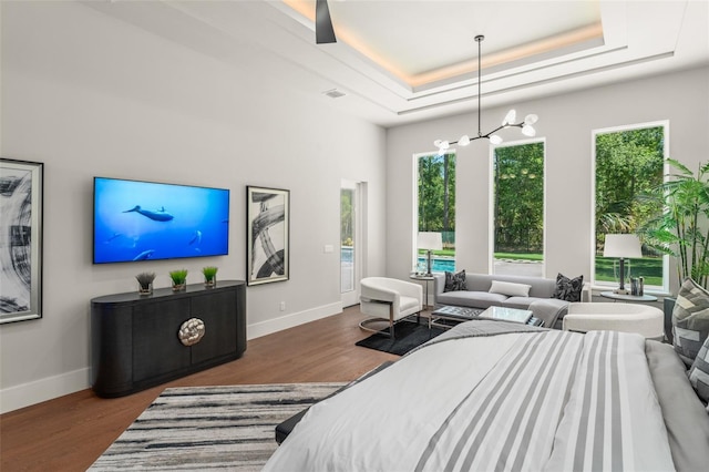 bedroom with a notable chandelier, a raised ceiling, visible vents, baseboards, and wood finished floors