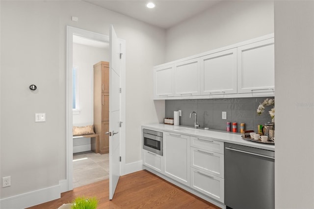 bar featuring a sink, light wood-style floors, oven, tasteful backsplash, and stainless steel dishwasher