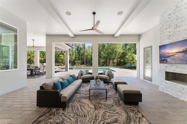 living room featuring beam ceiling, a large fireplace, a ceiling fan, and brick floor