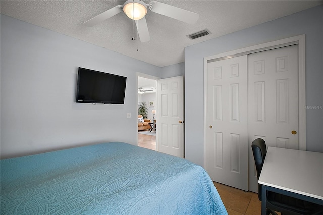 bedroom featuring a textured ceiling, light tile patterned floors, visible vents, a closet, and a ceiling fan