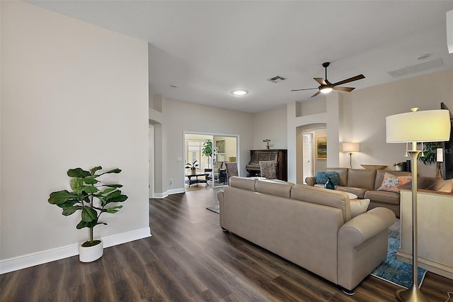 living area featuring dark wood finished floors, arched walkways, baseboards, visible vents, and a ceiling fan