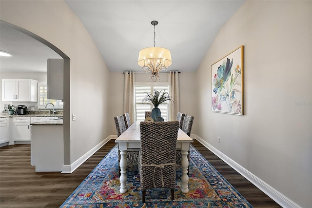 dining space with an inviting chandelier, baseboards, dark wood finished floors, and arched walkways