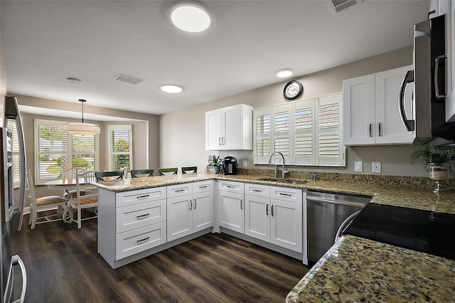 kitchen with light stone counters, appliances with stainless steel finishes, a sink, white cabinetry, and a peninsula