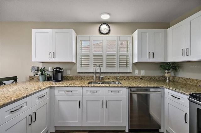 kitchen with light stone countertops, appliances with stainless steel finishes, white cabinets, a sink, and a peninsula