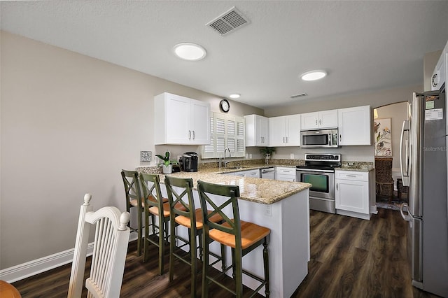 kitchen with a sink, appliances with stainless steel finishes, visible vents, light stone countertops, and a peninsula