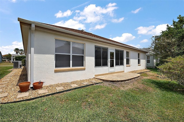 back of property with central AC unit, stucco siding, and a yard