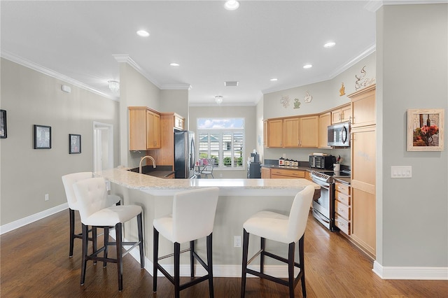 kitchen with a peninsula, appliances with stainless steel finishes, ornamental molding, and a breakfast bar