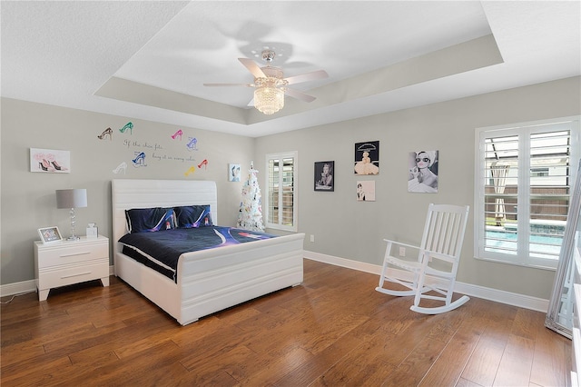 bedroom featuring baseboards, a raised ceiling, dark wood-type flooring, and ceiling fan