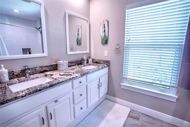 bathroom with double vanity, a sink, a shower, and baseboards