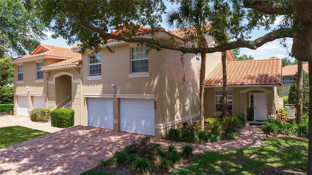 mediterranean / spanish home with a garage, stucco siding, decorative driveway, and a tiled roof