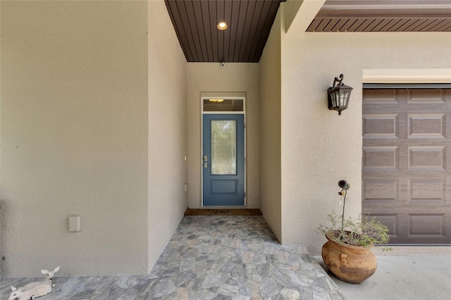 view of exterior entry featuring a garage, visible vents, and stucco siding