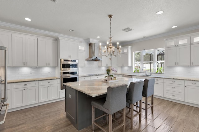kitchen with an inviting chandelier, appliances with stainless steel finishes, a sink, visible vents, and wall chimney exhaust hood