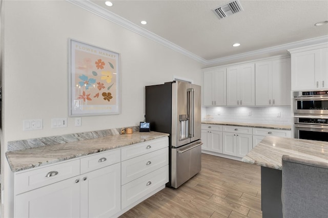 kitchen with appliances with stainless steel finishes, white cabinets, ornamental molding, light wood finished floors, and visible vents