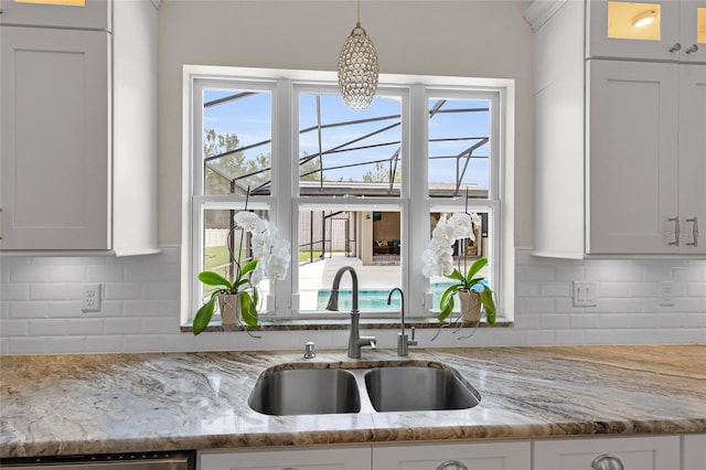 kitchen with tasteful backsplash, light stone counters, hanging light fixtures, and a sink