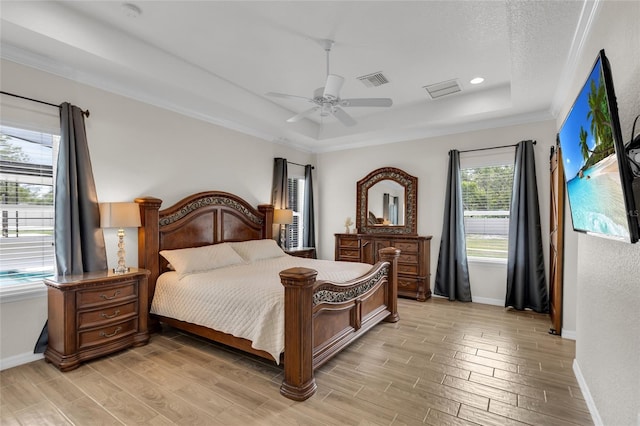 bedroom with visible vents, light wood-type flooring, a tray ceiling, and baseboards