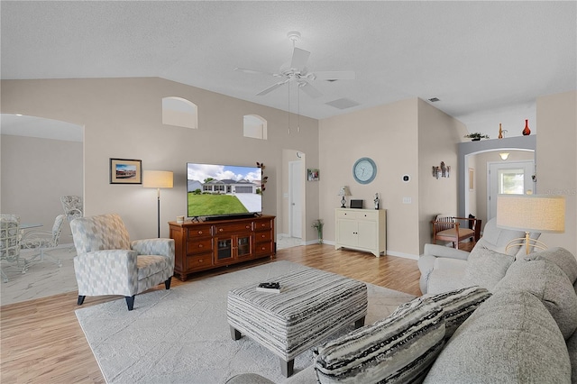 living room featuring ceiling fan, arched walkways, baseboards, wood finished floors, and vaulted ceiling