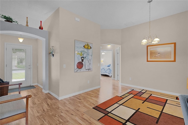 corridor featuring arched walkways, baseboards, an inviting chandelier, and light wood-style flooring