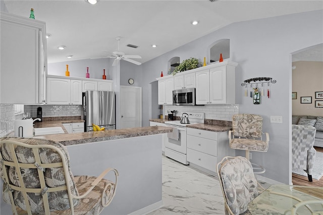 kitchen featuring a sink, stainless steel appliances, a ceiling fan, a peninsula, and vaulted ceiling