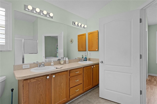 ensuite bathroom with double vanity, a sink, and a textured ceiling