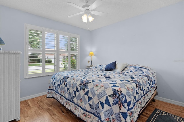 bedroom with a ceiling fan, baseboards, wood finished floors, and a textured ceiling