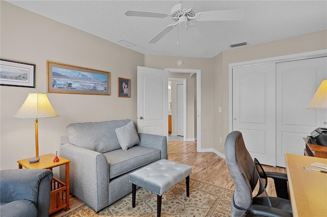 office area with a ceiling fan, a textured ceiling, visible vents, baseboards, and light wood-style flooring