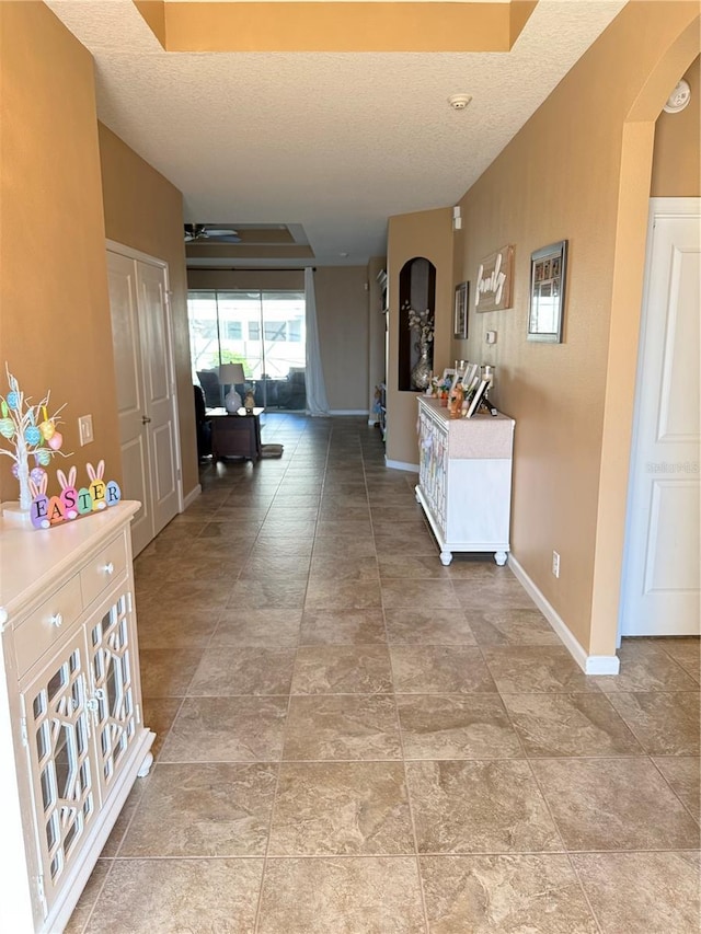 corridor with a textured ceiling, baseboards, and arched walkways