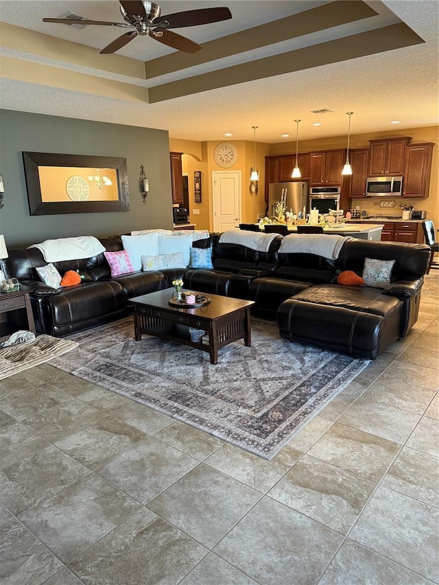 living room with a ceiling fan and a tray ceiling