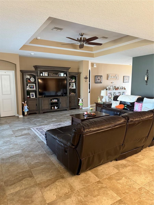 living room featuring a textured ceiling, visible vents, ceiling fan, and a raised ceiling