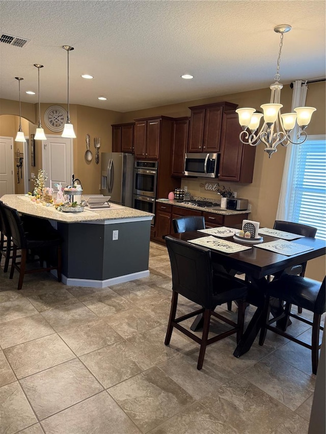 2504 Cavender Creek Rd, Minneola, FL 34715 - kitchen featuring appliances with stainless steel finishes, a chandelier, dark brown cabinets, a kitchen island with sink, and hanging light fixtures