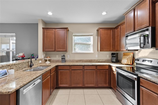 kitchen featuring light stone countertops, a sink, light tile patterned floors, a peninsula, and appliances with stainless steel finishes