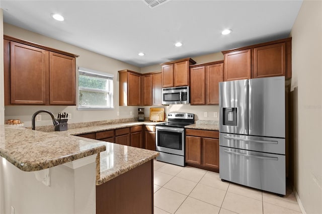 kitchen featuring light tile patterned floors, brown cabinetry, light stone counters, a peninsula, and appliances with stainless steel finishes