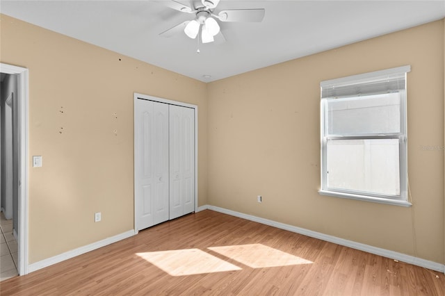 unfurnished bedroom featuring baseboards, ceiling fan, a closet, and light wood-style flooring