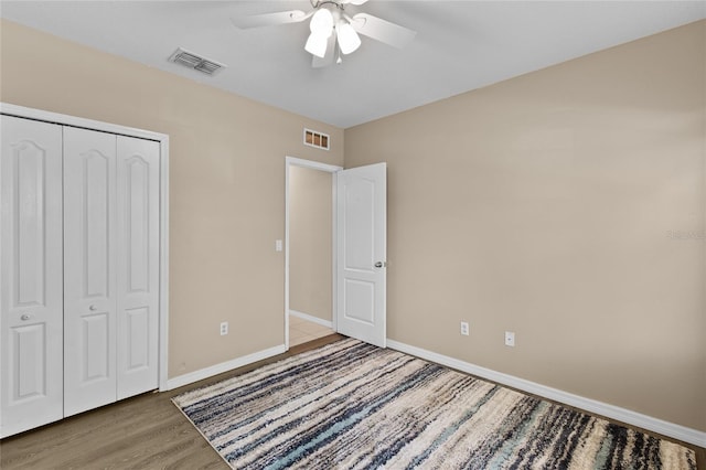 unfurnished bedroom with a closet, visible vents, wood finished floors, and baseboards