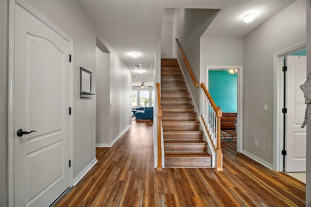 stairs featuring a textured ceiling, visible vents, wood finished floors, and baseboards