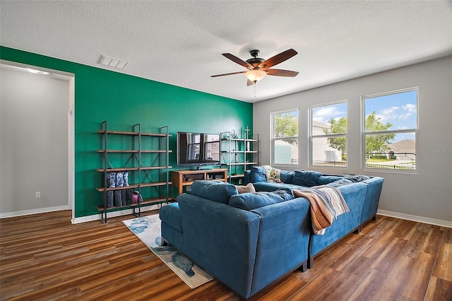 living room with a textured ceiling, ceiling fan, visible vents, baseboards, and wood finished floors