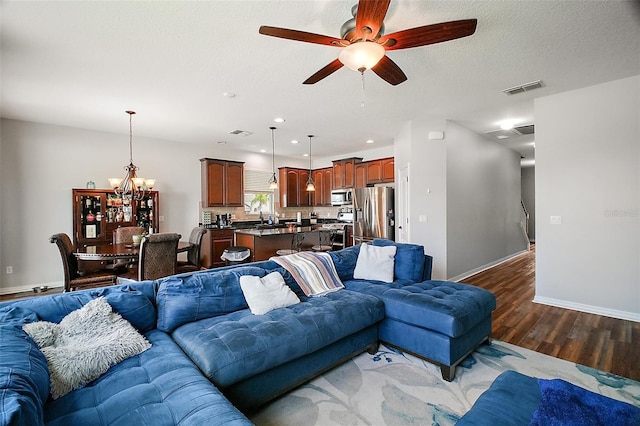 living area featuring baseboards, visible vents, wood finished floors, and ceiling fan with notable chandelier